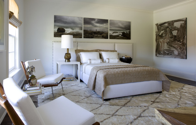a sophisticated bedroom with a creamy bed, a white stand and a black round table, chic white chairs and some art