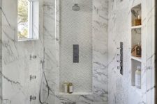 a sophisticated white marble walk-in shower with a brown floor and a small window plus glass doors