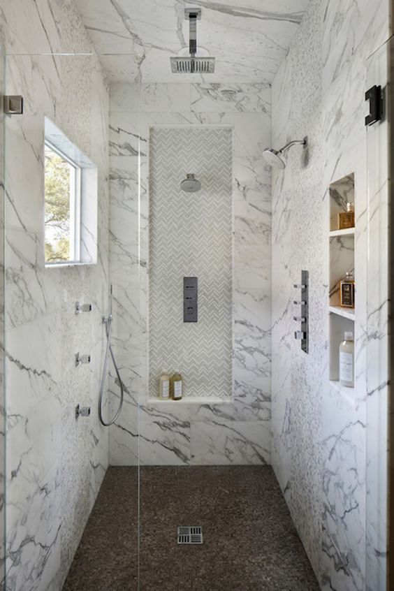 a sophisticated white marble walk-in shower with a brown floor and a small window plus glass doors
