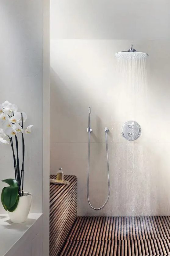 a spa-inspired wlak-in shower with wooden slabs covering the floor and the bench, with a rain shower and an orchid