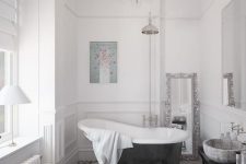 a stylish French style bathroom with a mosaic floor, elegant chandelier, a clawfoot tub, a side table and lamps