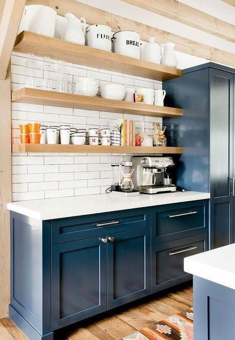 a stylish navy farmhouse kitchen with blonde wood beams and shelves, white countertops and white skinny tiles