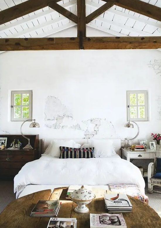 a vintage-infused bedroom with a white bed and bedding, a table as a nightstand and a stained dresser that acts as a nightstand, too