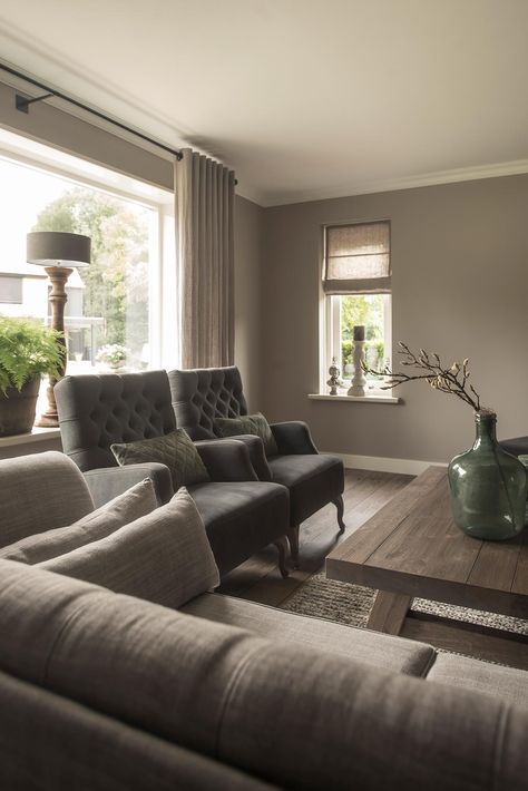 a vintage inspired taupe living room with a grey sofa and graphite grey vintage chairs, a wooden coffee table and neutral curtains