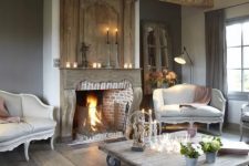 a vintage living room with a brick fireplace, a large wooden beam, grey and creamy vintage furniture, light-stained floors and a whitewashed coffee table