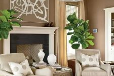 a welcoming taupe living room with a vintage-styled fireplace, tan chairs, a woven coffee table, statement potted plants and polka dot pillows