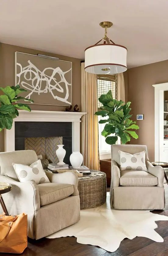 a welcoming taupe living room with a vintage styled fireplace, tan chairs, a woven coffee table, statement potted plants and polka dot pillows