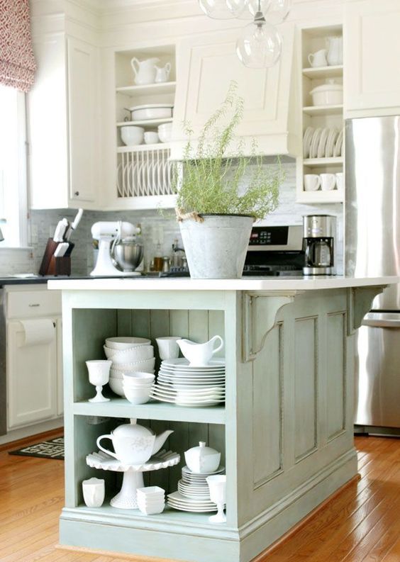 a white cottage kitchen with shaker style cabinets, a mint green kitchen island with open shelves for storage and stainless steel appliances