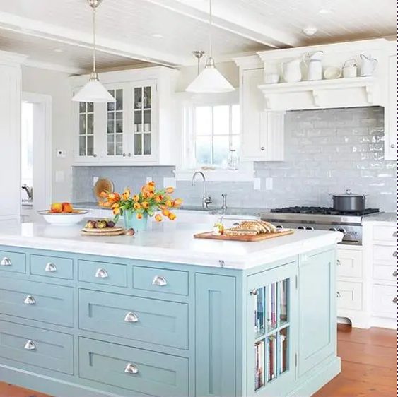 a white farmhouse kitchen with a glossy white tile backsplash, a serenity blue kitchen island with book storage and drawers is a smart idea and a touch of color