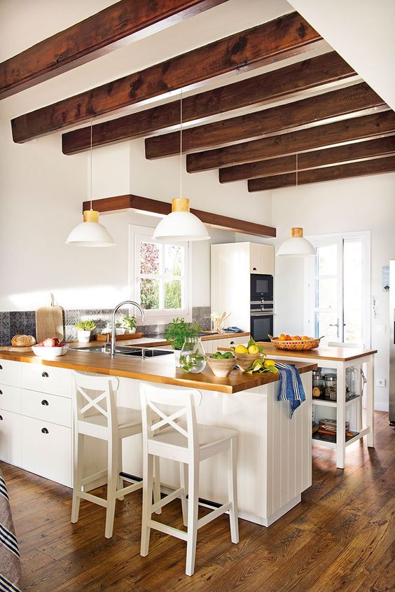 a white farmhouse kitchen with planked cabinets and butcherblock countertops, a kitchen island with open shelves and stained wooden beams on the ceiling