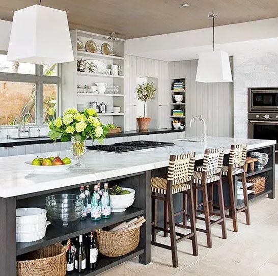 a white farmhouse kitchen with planked cabinets and walls, built-in appliances and an oversized grey kitchen island with a dining space and lots of open shelves for storage