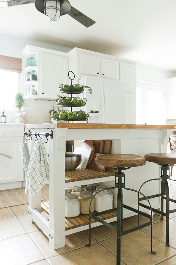 a white farmhouse kitchen with shaker cabinets, a small kitchen island with open shelves and a closed storage compartment