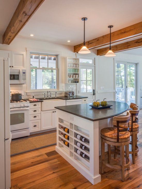 a white farmhouse kitchen with shaker style cabinets, black countertops, a rounded kitchen island with wine storage