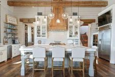 a white farmhouse kitchen with white cabinets, a refined kitchen island, a reclaimed wooden floor, light-stained wooden beams and a ceiling