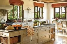 an adorable farmhouse kitchen with wooden beams on the ceiling, neutral cabinets, black countertops and a tan kitchen island with drawers and crates for storage