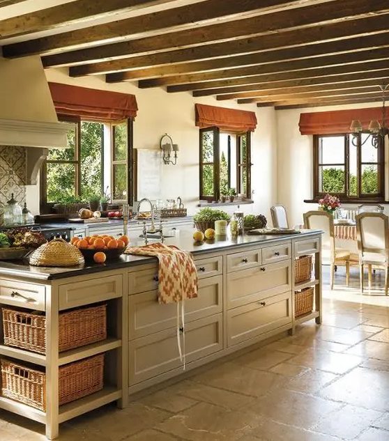 an adorable farmhouse kitchen with wooden beams on the ceiling, neutral cabinets, black countertops and a tan kitchen island with drawers and crates for storage