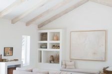 an airy living room with blonde wood beams, neutral furniture and built-in shelves, printed textiles and a niche with a basket