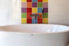 an elegant bathroom clad with white square tiles and with a multi color accent to highlight the bathtub