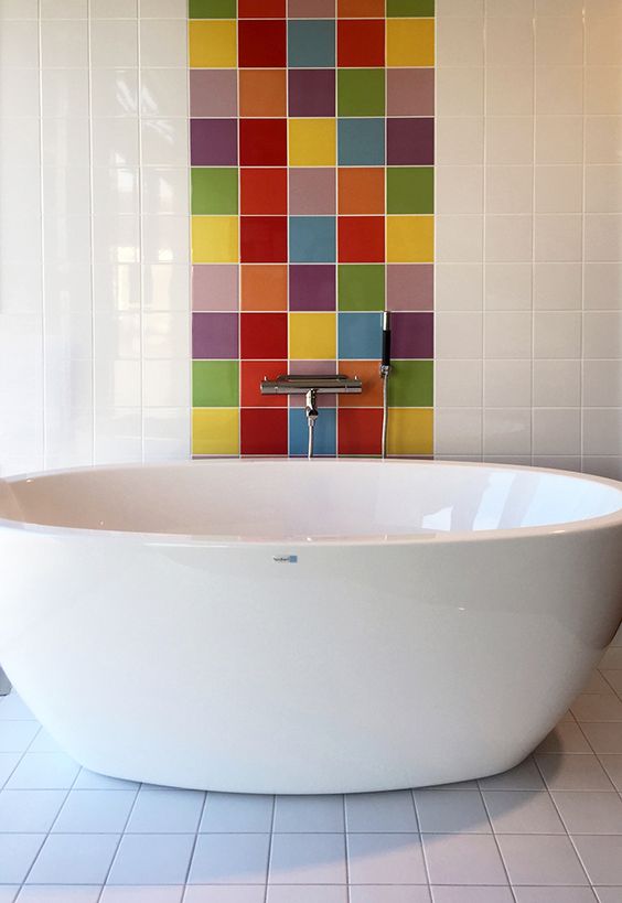 an elegant bathroom clad with white square tiles and with a multi color accent to highlight the bathtub