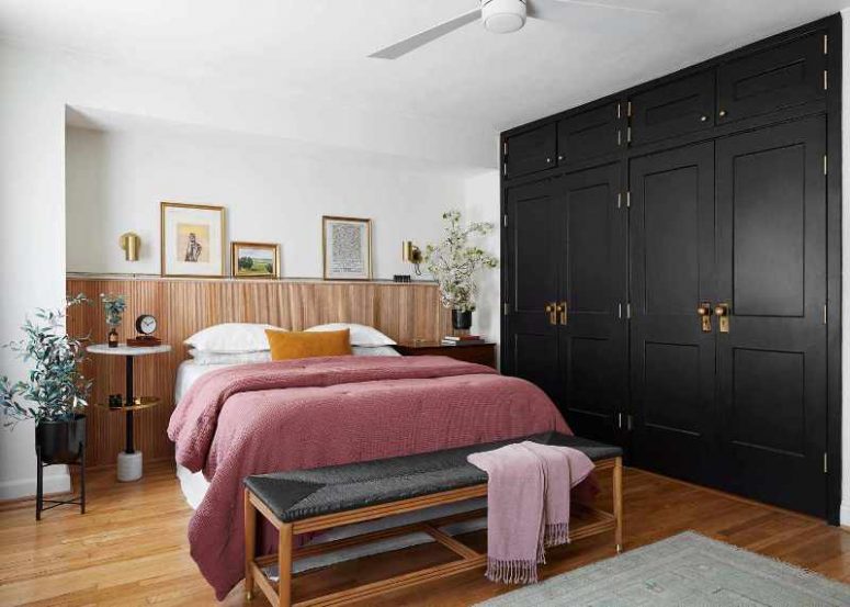 an elegant modern bedroom with a black closet, a bed and a woven bench, a round tiered table and a stained nightstand