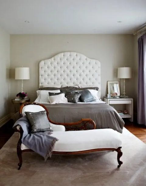 an elegant vintage-inspired bedroom with a creamy bed with an extended headboard, a chic daybed, a vintage side table and a modern white nightstand