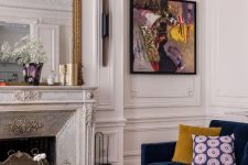 an exquisite living room with an antique fireplace, a navy sofa with bold pillows, a bright artwork and layered coffee tables