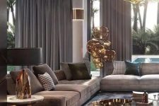 an exquisite taupe living room with taupe sofas and curtains, a brown rug, a glass and metal coffee table and a gorgeous chandelier