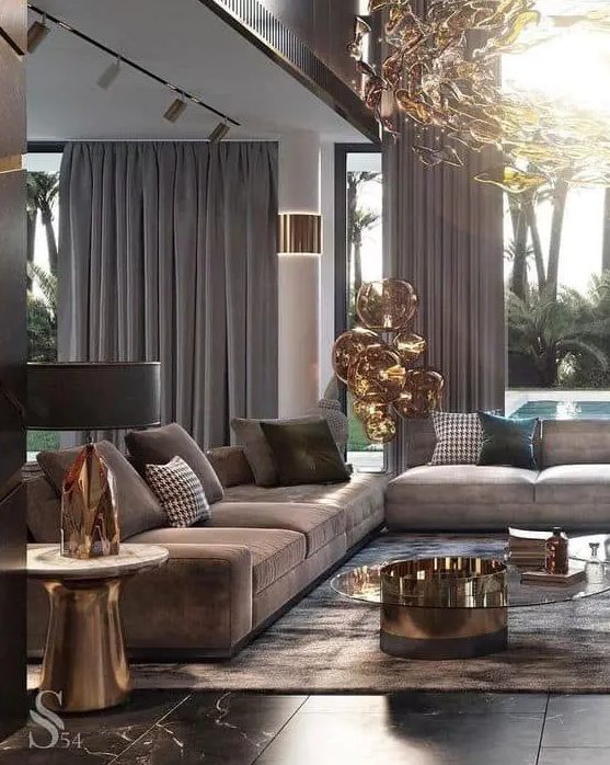 an exquisite taupe living room with taupe sofas and curtains, a brown rug, a glass and metal coffee table and a gorgeous chandelier
