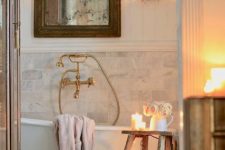 an inspiring French bathroom with a white marble tile wall, a vintage mirror, a clawfoot tub, pillars and crystal lamps and chandeliers
