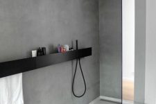 an ultra-minimalist bathroom clad with concrete, with a black shelf and shower and a glass partition that is seamless