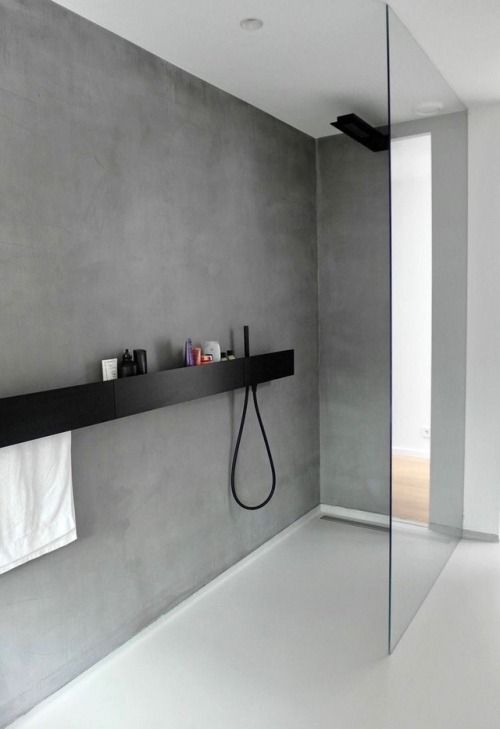 an ultra minimalist bathroom clad with concrete, with a black shelf and shower and a glass partition that is seamless