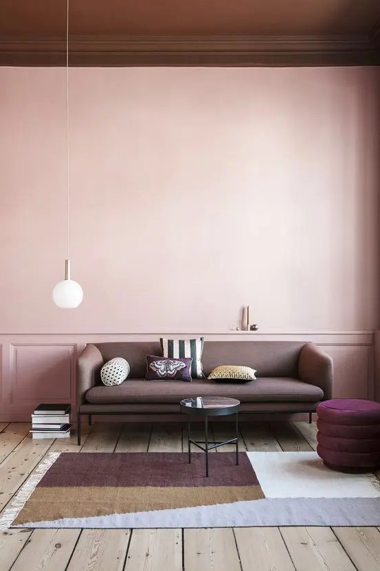 a beautiful pastel living room with pink walls, a dusty pink sofa, a purple pouf, a side table, a color block rug and some negative space to feel relaxed here