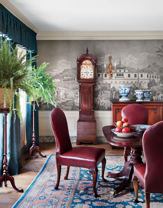 a beautiful vintage dining room with a mural, a rich-stained dining table, burgundy leathr chairs, a stained credenza, teal curtains and greenery plus a grandfather clock