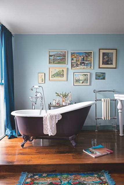 a blue bathroom with a purple clawfoot bathtub on a platform, a gallery wall, blue textiles, a vintage free-standing sink