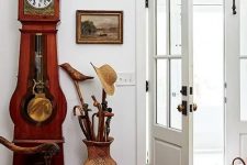 05 a chic entryway with a red wood clock, a wicker vase for umbrellas and a refined chair