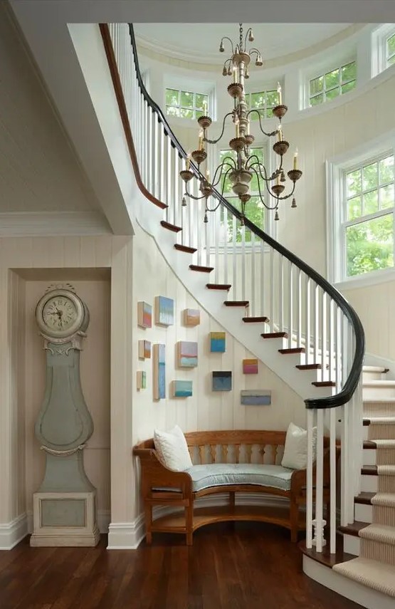 a coastal entryway with a dusty blue grandfather's clock and a rounded bench, a color block gallery wall and a vintage chandelier