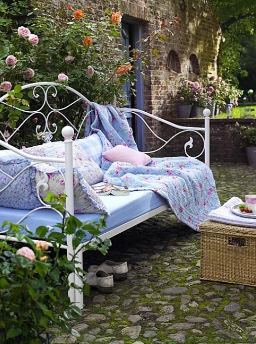 a vintage inspired white forged daybed with many pillows and a floral blanket is timeless classics for an elegant garden