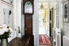 07 a farmhouse space with white walls, a dark-stained grandfather clock, a bold printed rug, a dark-stained console table and a gallery wall