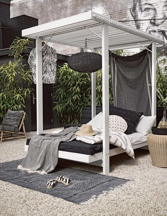 a cabana style wooden daybed with a hanging black lamp, a curtain and lot sof pillows and blankets welcomes with its look