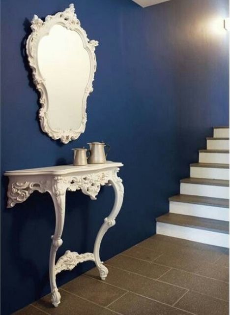 a navy wall and a contrasting vintage carved half console table, a matching mirror for adding a refined vintage feel to the space
