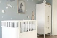 a dreamy Scandi nursery with pale blue walls and an accent one, white furniture, pendant lamps and a mobile plus toys