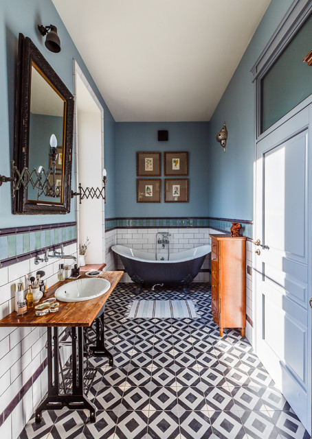 a gorgeous vintage bathroom done in blue, with a black and white tile floor, a navy clawfoot bathtub, stained furniture, artwork and a mirror
