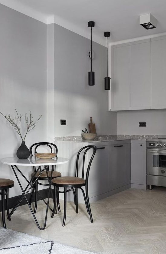 a minimalist grey Nordic kitchen with black pendant lamps, a grey stone countertop and a table with hairpin legs