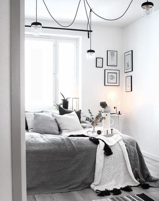 a monochromatic Scandi bedroom with a bed with grey and white bedding, some lamps, lights and a gallery wall