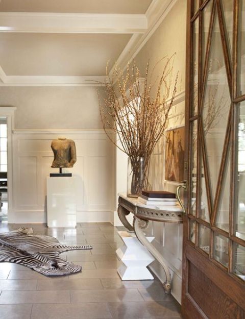 a sophisticated vintage entryway with a refined grey half table, with an arrangement of branches, gorgeous artwork and a zebra print rug