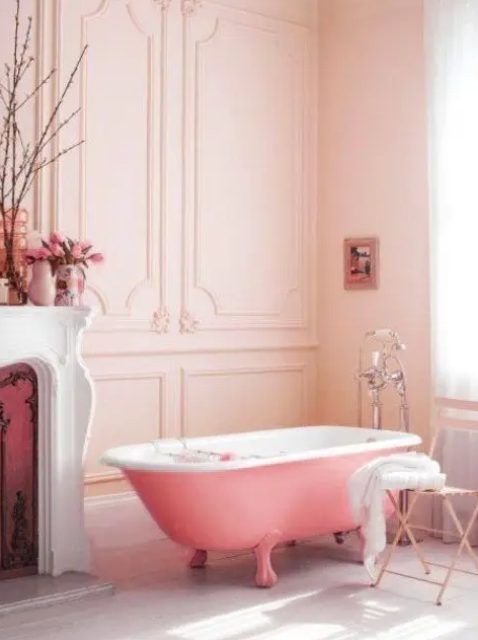 a lovely girlish bathroom with blush paneled walls, a vintage fireplace, a pink clawfoot bathtub, a shabby chic chair and some blooms