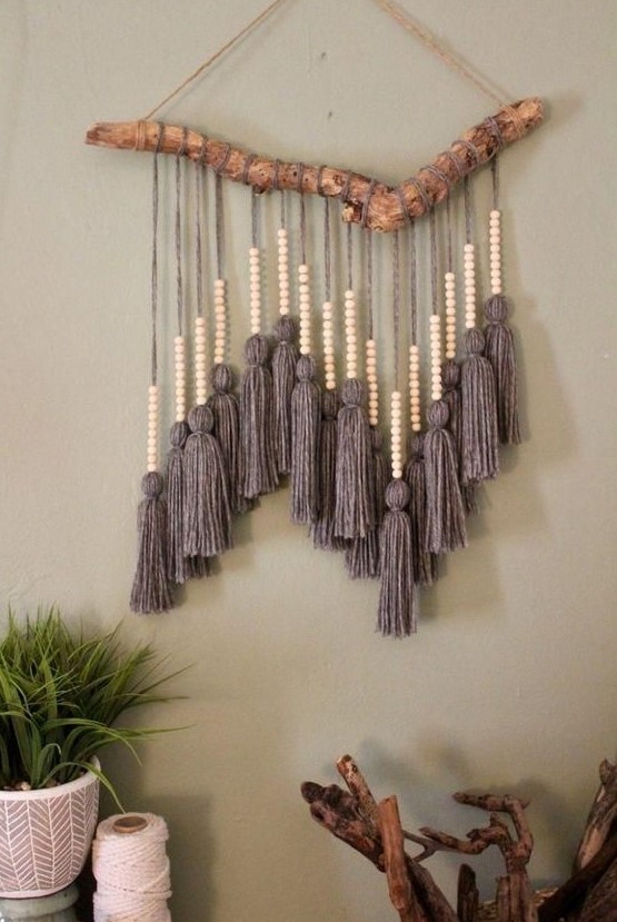 a cool boho wall hanging with large grey tassels and wooden beads and a natural branch is very bold