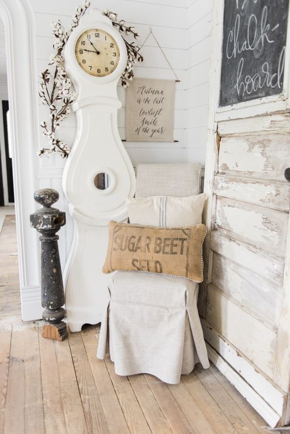 a neutral shabby chic space with a white grandfather clock, a neutral chair and a printed pillow, a chalkboard and some vintage decor