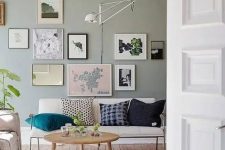 19 a Nordic living room with a pale green accent wall, a creamy loveseat, a gallery wall, a sconce, a round table and neutral rugs