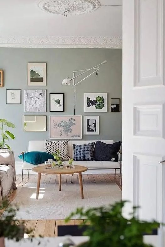 a Nordic living room with a pale green accent wall, a creamy loveseat, a gallery wall, a sconce, a round table and neutral rugs